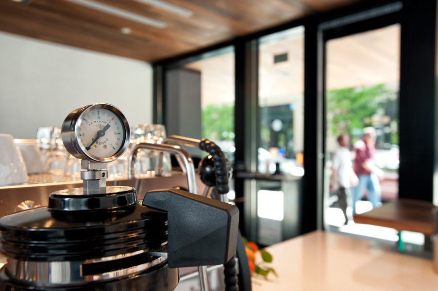 A close-up photo of coffee making equipment at Little Owl Coffee on a counter with windows and blurred people outside visible