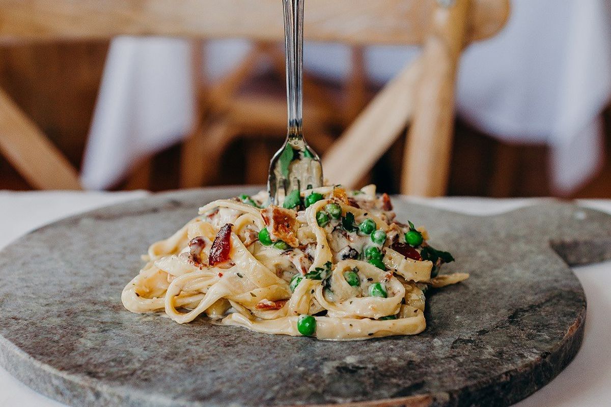 A pile of carbonara on a granite serving board with a fork stuck in it, upright.