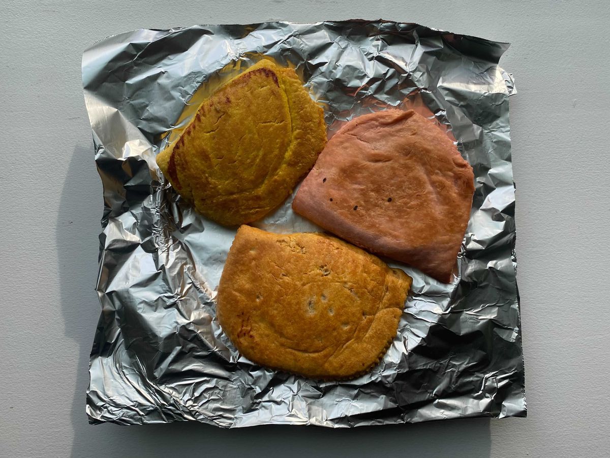 An overhead photograph of three colorful patties on aluminum foil.