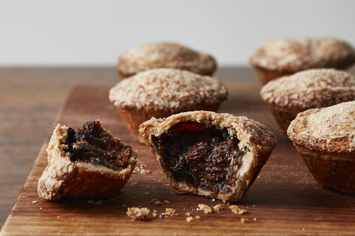 Six mince pies on a wooden chopping board, with a cut-through on one in the foreground.