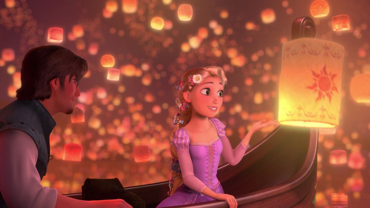 Rapunzel, a young woman with long blonde hair wearing a pink dress, sits in a boat surrounded by floating paper lanterns and admires one up close while would-be thief Flynn Rider sits in the boat and watches her in Disney’s Tangled