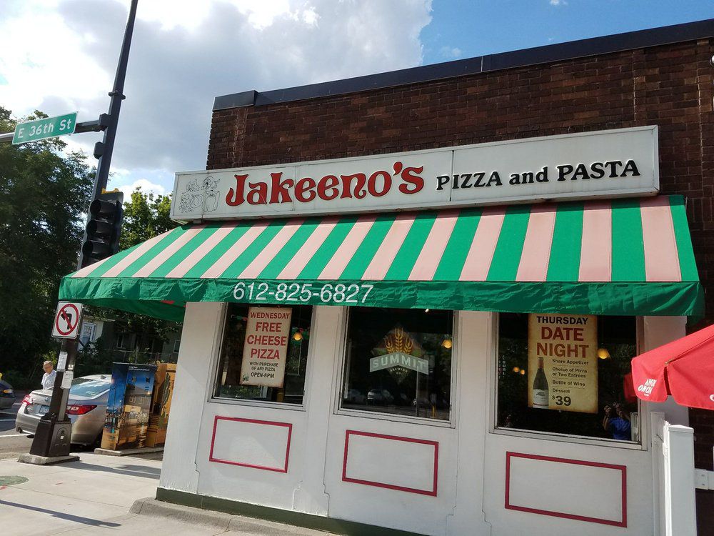 The exterior of a restaurant with a sign that says Jakeeno’s and a green and white-striped awning. 
