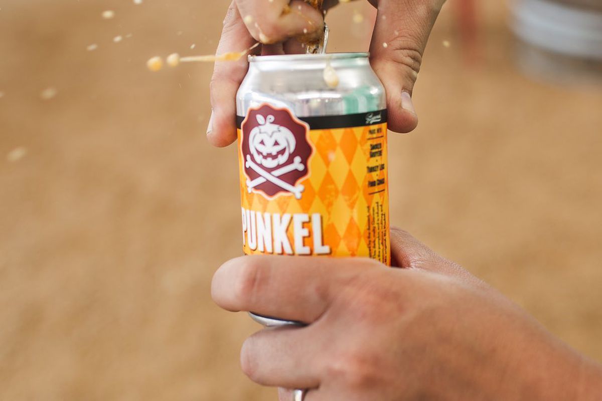 Two hands holding a can of beer labeled “Punkel.” One hand is steadying the bottom while the other opens the pull tab of the beer. 