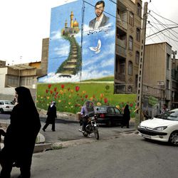 In this Tuesday, May 28, 2013 photo, Iranian pedestrians make their way under a mural showing Ali Asghar Dehnadi, who was killed during the 1980-88 Iran-Iraq war, in downtown Tehran, Iran.