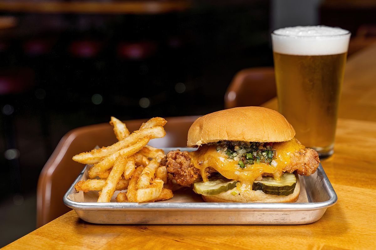 A fried chicken sandwich and fries with a pint of beer.