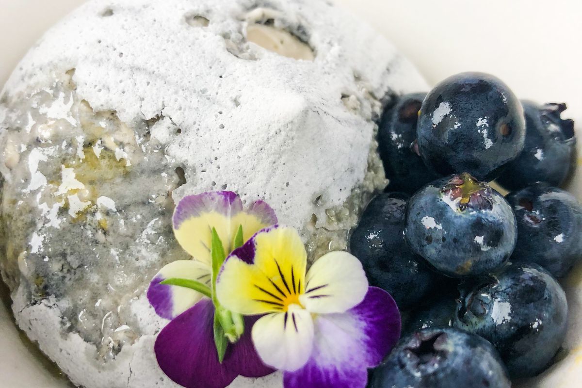 A picture of a meringue-looking pavlova with an edible flower and fresh blueberries