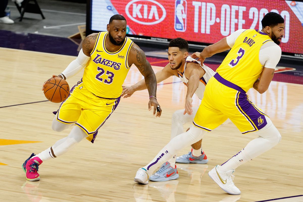 LeBron James of the Los Angeles Lakers drives the ball as Anthony Davis sets a pick on Devin Booker of the Phoenix Suns during the first half of the NBA preseason game at Talking Stick Resort Arena on December 18, 2020 in Phoenix, Arizona.