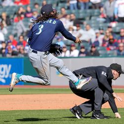 APRIL 09: Seattle Mariners shortstop J.P. Crawford (3) throws to first base for an out as umpire Nate Tomlinson (114) ducks out of the way of the throw during the tenth inning of the Major League Baseball game between the Seattle Mariners and Cleveland Guardians on April 9, 2023, at Progressive Field in Cleveland, OH.