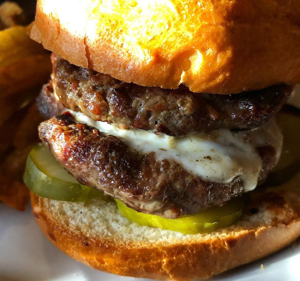 A close-up on a double stacked burger with white, melty cheese