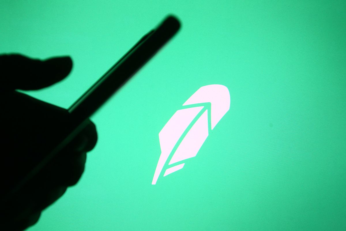 A hand holding a cellphone with the Robinhood logo in the background.