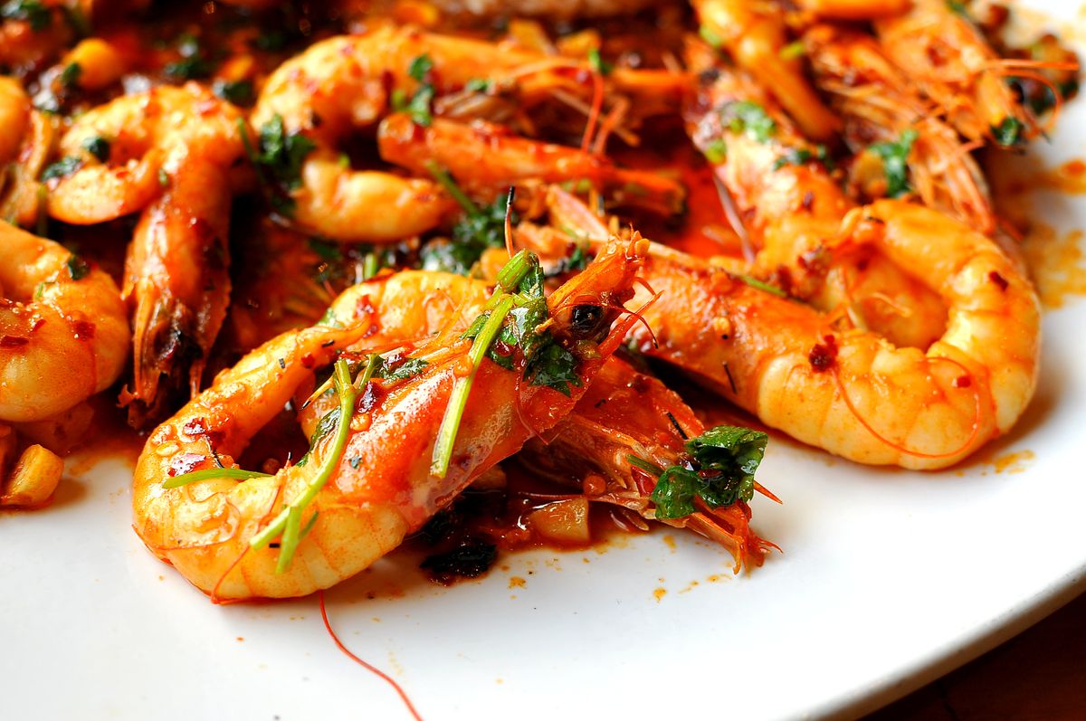 A serving of drunken shrimp garnished with herbs on a round, white plate.
