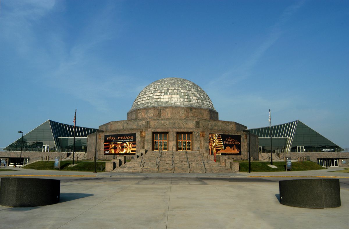 The exterior of the Adler Planetarium building in Chicago.  The top is dome shaped and there are pyramid shaped structures on both sides of the building. 
