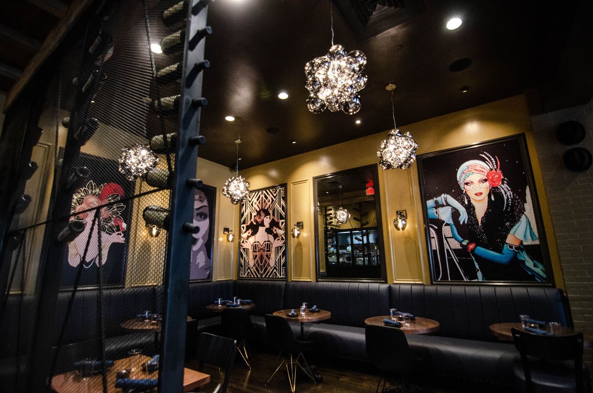 A dimly lit restaurant interior with black leather banquettes features large paintings of women wearing Prohibition-era outfits.