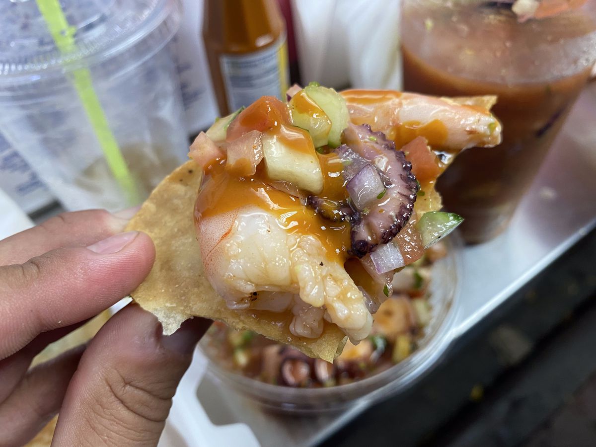 An octopus tendril and a piece of cooked shrimp are scooped on a tostada.