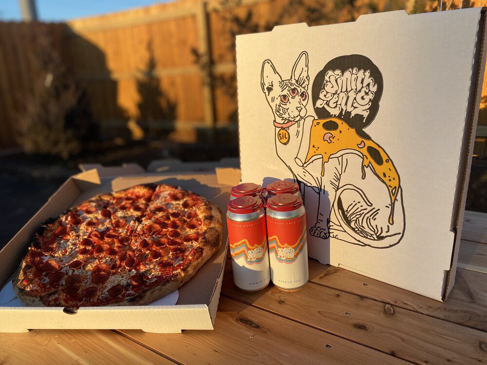 The outside of a pizza box shows the name Smith &amp; Lentz and an image of a three-eyed furless cat wearing a slice of pizza on its back. Next to that are a four-pack of beer cans and an open pizza box with a large pepperoni pizza inside.