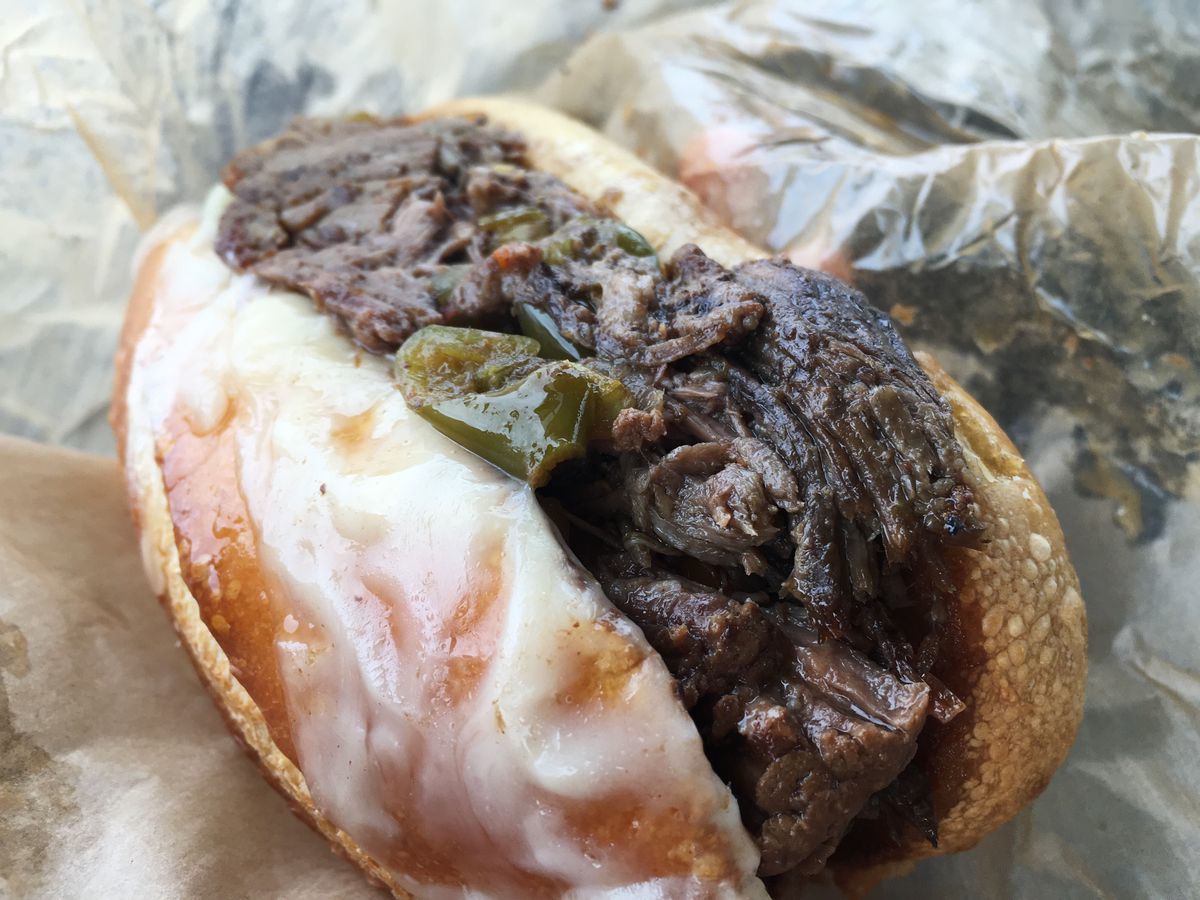 An Italian beef sandwich with cheese melted over the roll on greasy wax paper.