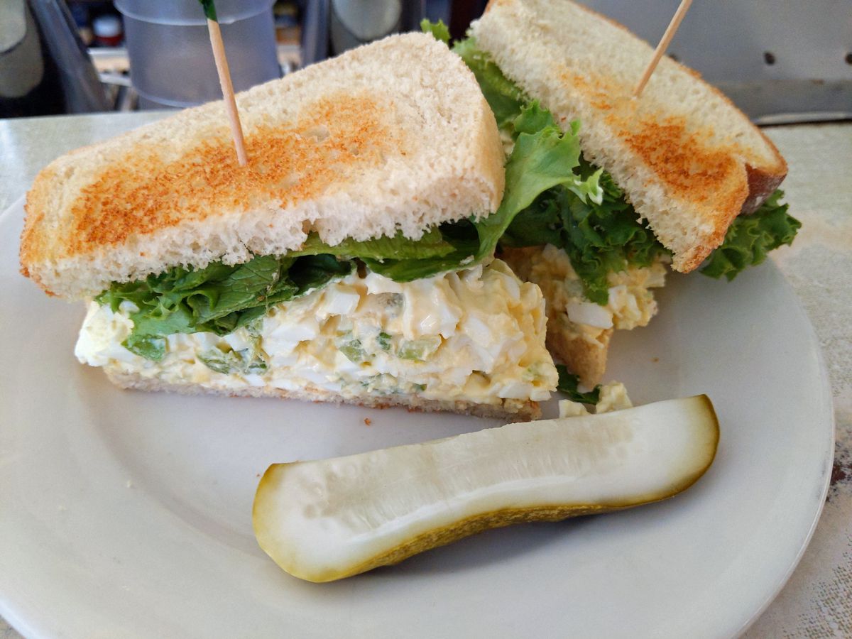 A white bread sandwich browned from the toaster with lettuce and egg salad, in two halves.