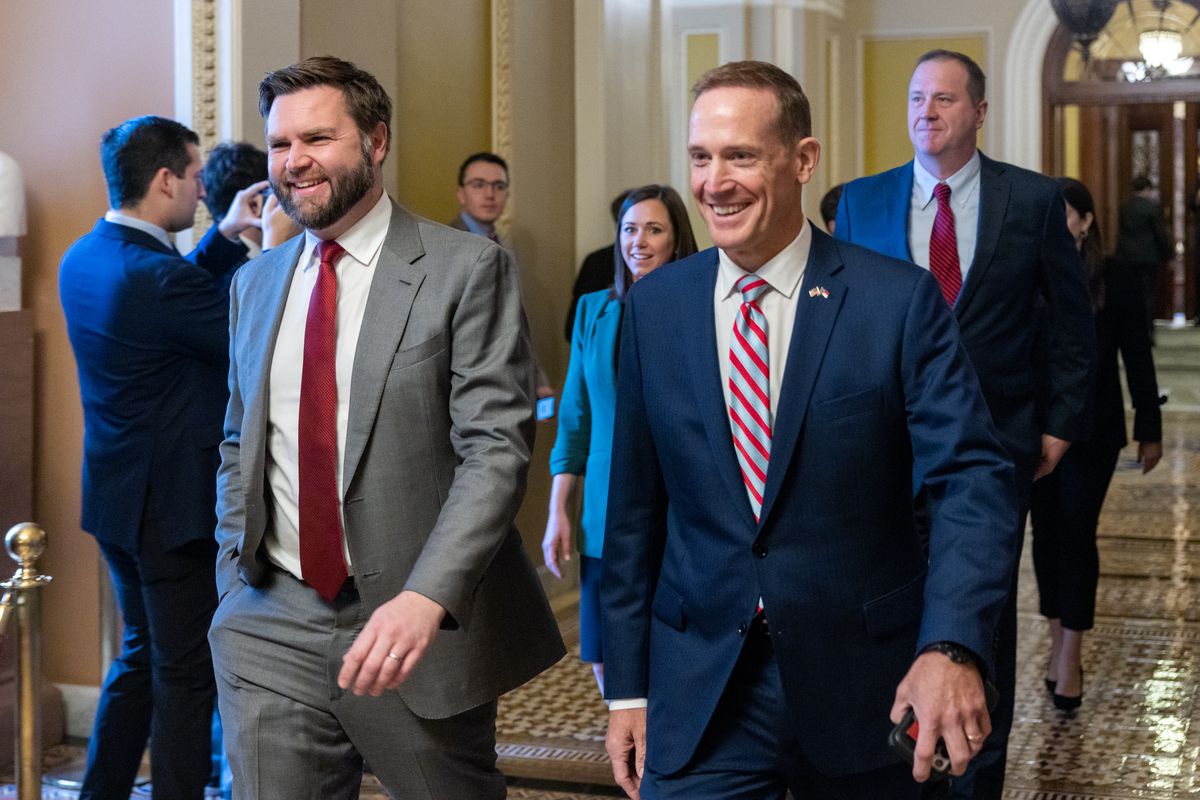 JD Vance and Ted Budd smile as they walk side-by-side through a hallway featuring arched doors and a gold and brown tile mosaic floor.