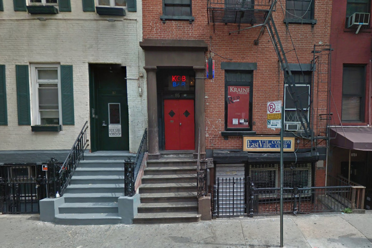 An exterior shot of KGB Bar in a brick townhouse with a red and blue neon sign lit up.