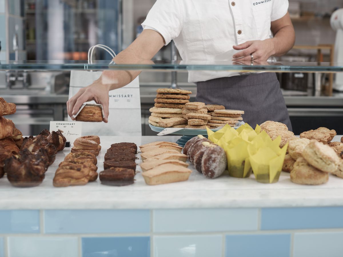 Behind a glass case, cookies and pastries are lined up and a chef places them.