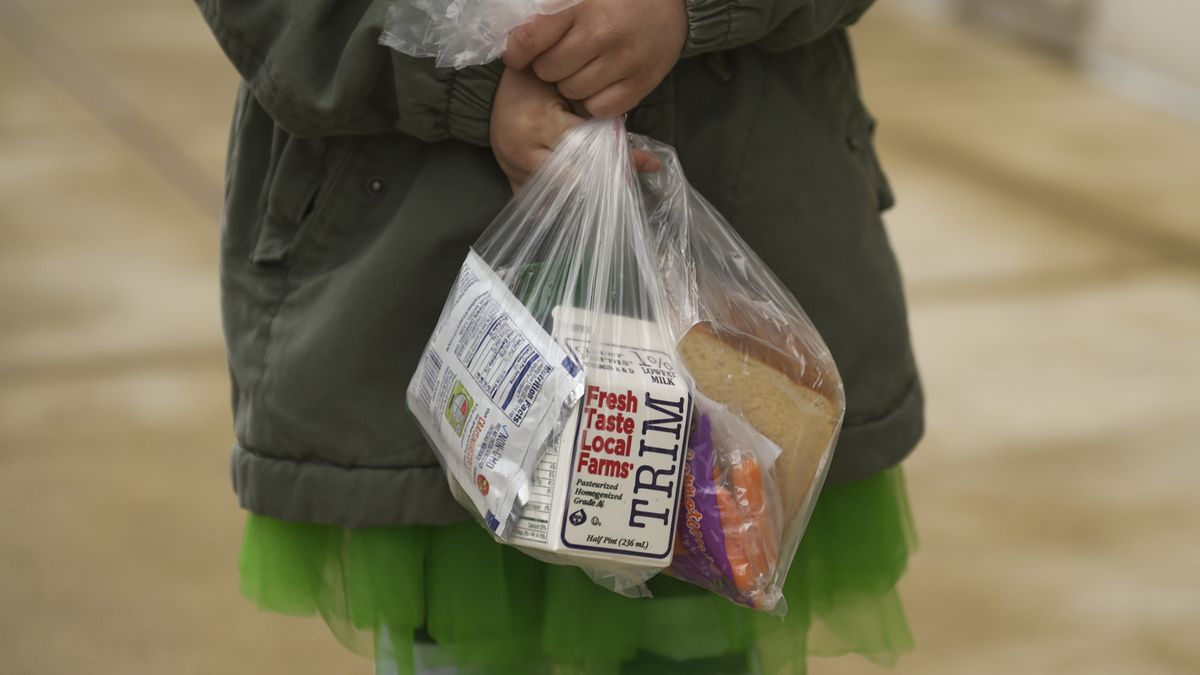 Child holds a plastic bag containing a carton of milk and other breakfast foods.
