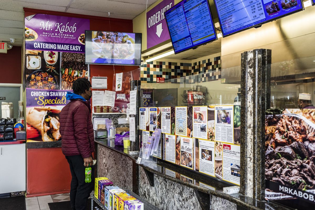 Man considers the menu while standing at a counter; a digital menu board hangs above.