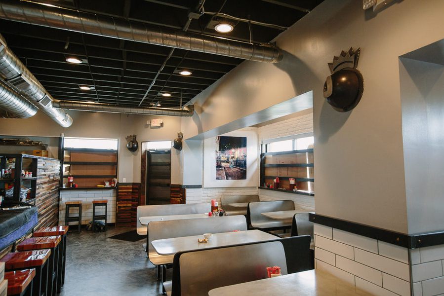 The interior of Johnny Noodle King has fast-food type tables, a bar with reclaimed wood on the exterior and red stools, and white subway tile on the walls. 