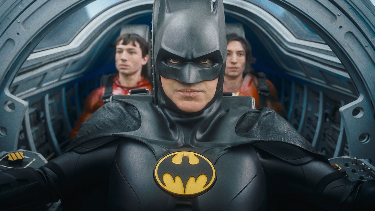 (L-R) Ezra Miller as The Flash, Michael Keaton as Batman and Ezra Miller as The Flash in The Flash. They’re in the cramped cockpit of the Batwing, with Batman in the pilot’s seat and the two Flashes sitting next to each other behind him.