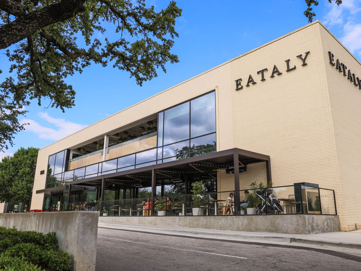 The exterior corner of a large building in cream-colored brick expansive windows and a sign that reads “Eataly.”