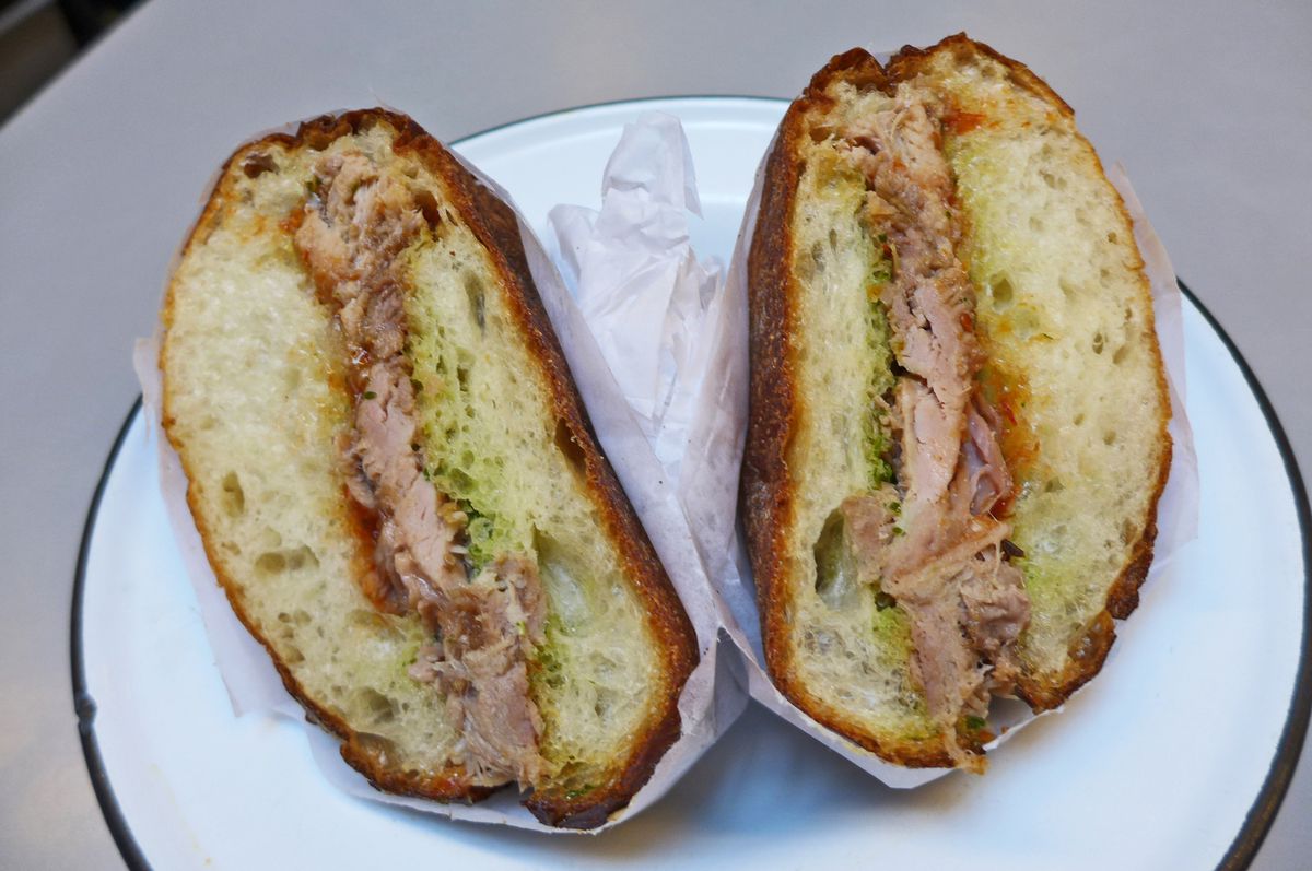 A roll stuffed with roast pork seen in cross section, both halves wrapped in white butcher paper.