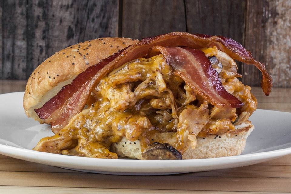 A sandwich overflowing with saucy chicken and two slices of bacon across the top.