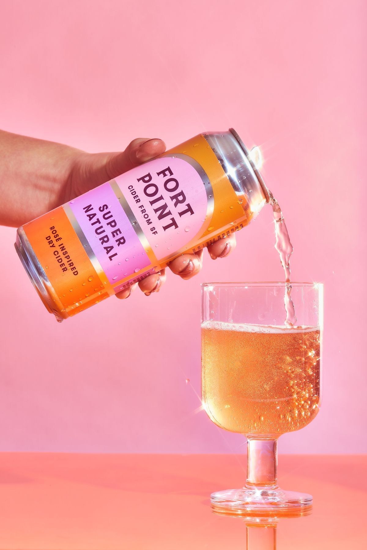 A can of pink-colored beverage being poured into a glass.