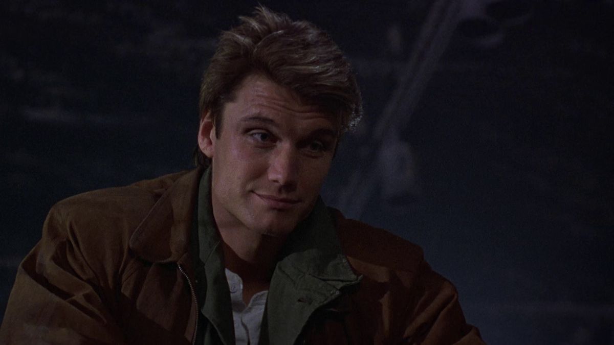 Dolph Lundgren looks very handsome in Dark Angel, wearing a brown coat and smiling slightly.