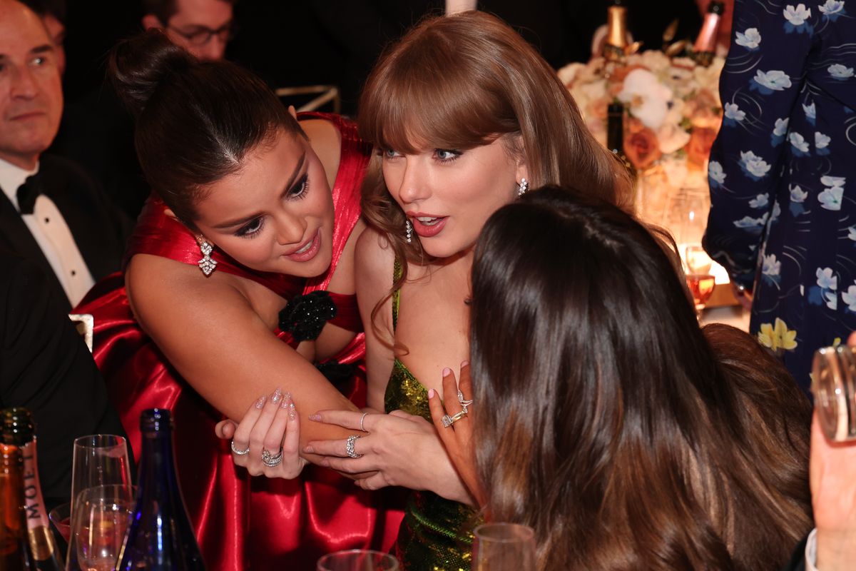 Selena Gomez and Taylor Swift leaning close and talking.