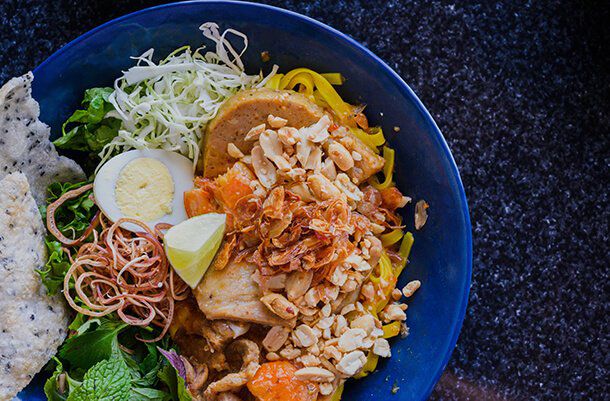 A close up overhead shot of a blue bowl with lots of Vietnamese noodles and other ingredients inside.