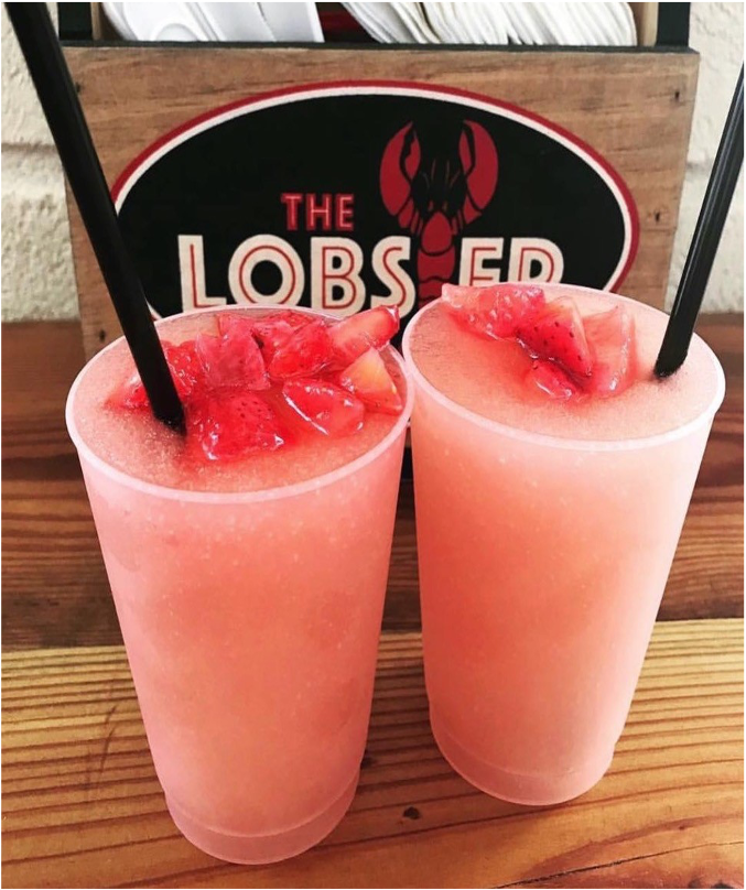 Two pink slushee cocktails in plastic cups topped with strawberry slices