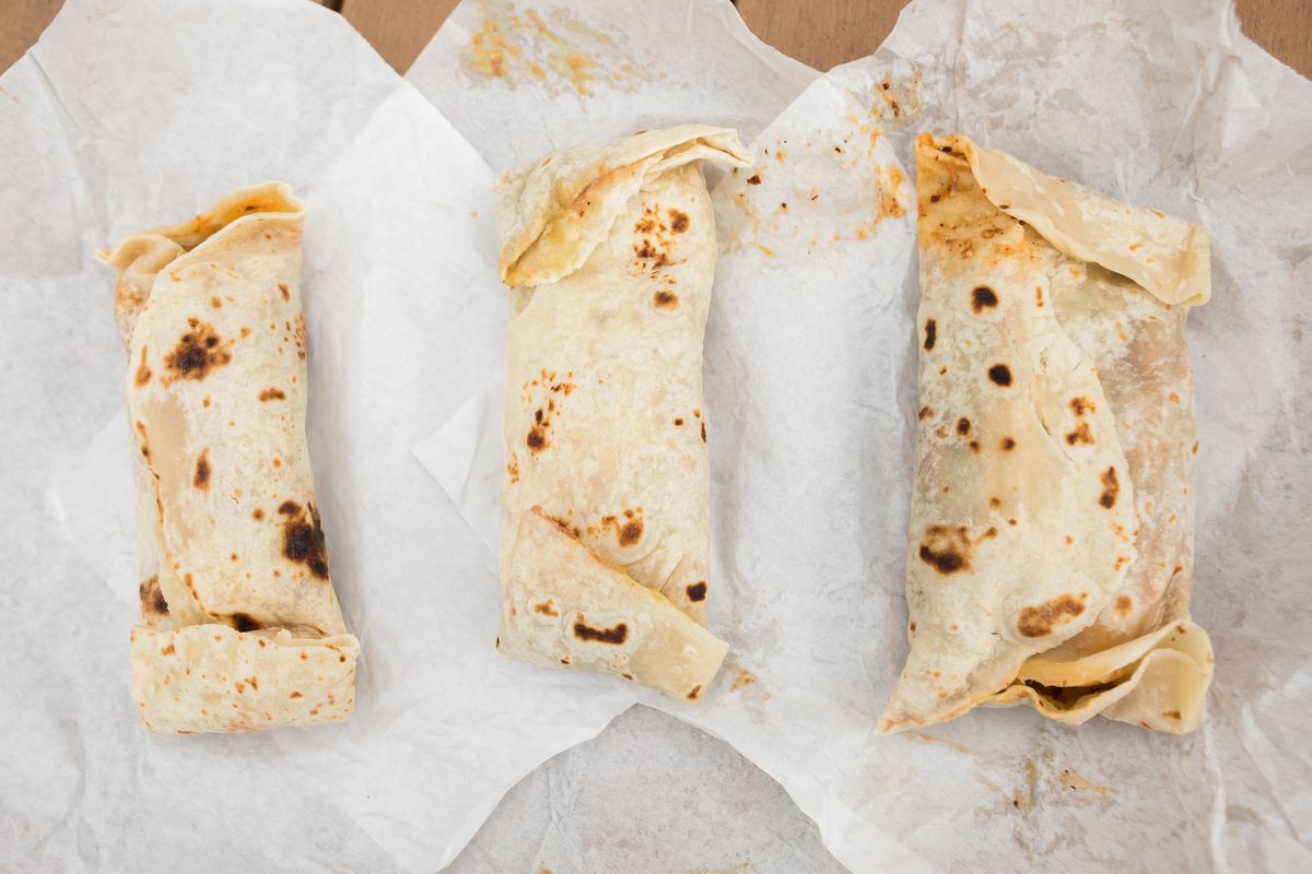 Three burritos from El Charrito are displayed atop its parchment paper wraps, with a charred flour tortilla exterior.