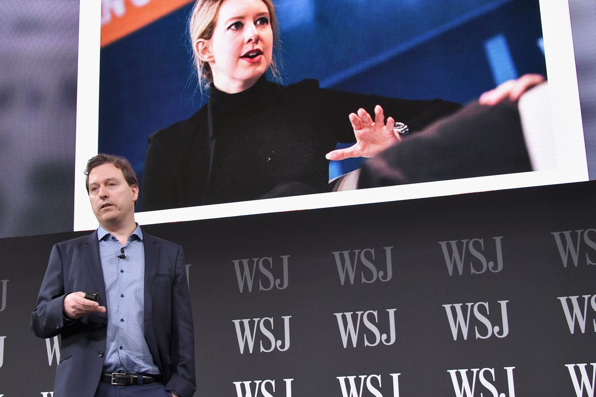Writer John Carreyrou in front of a screen showing Theranos founder Elizabeth Holmes