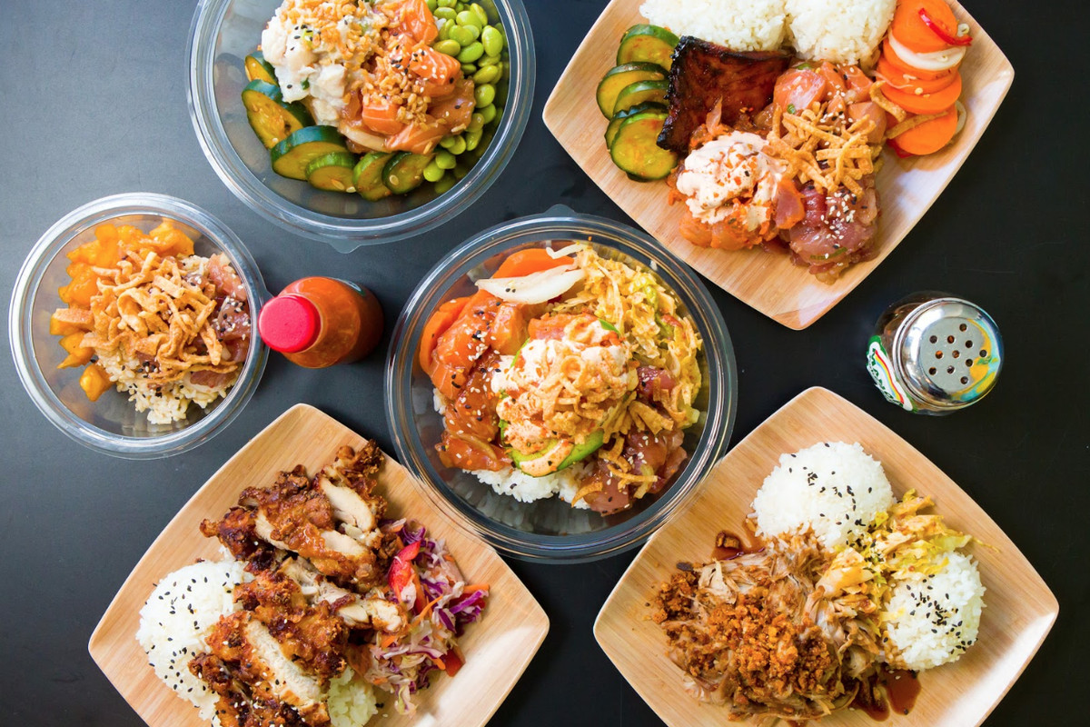 Overhead view of multiple restaurant dishes, including poke, on a dark table