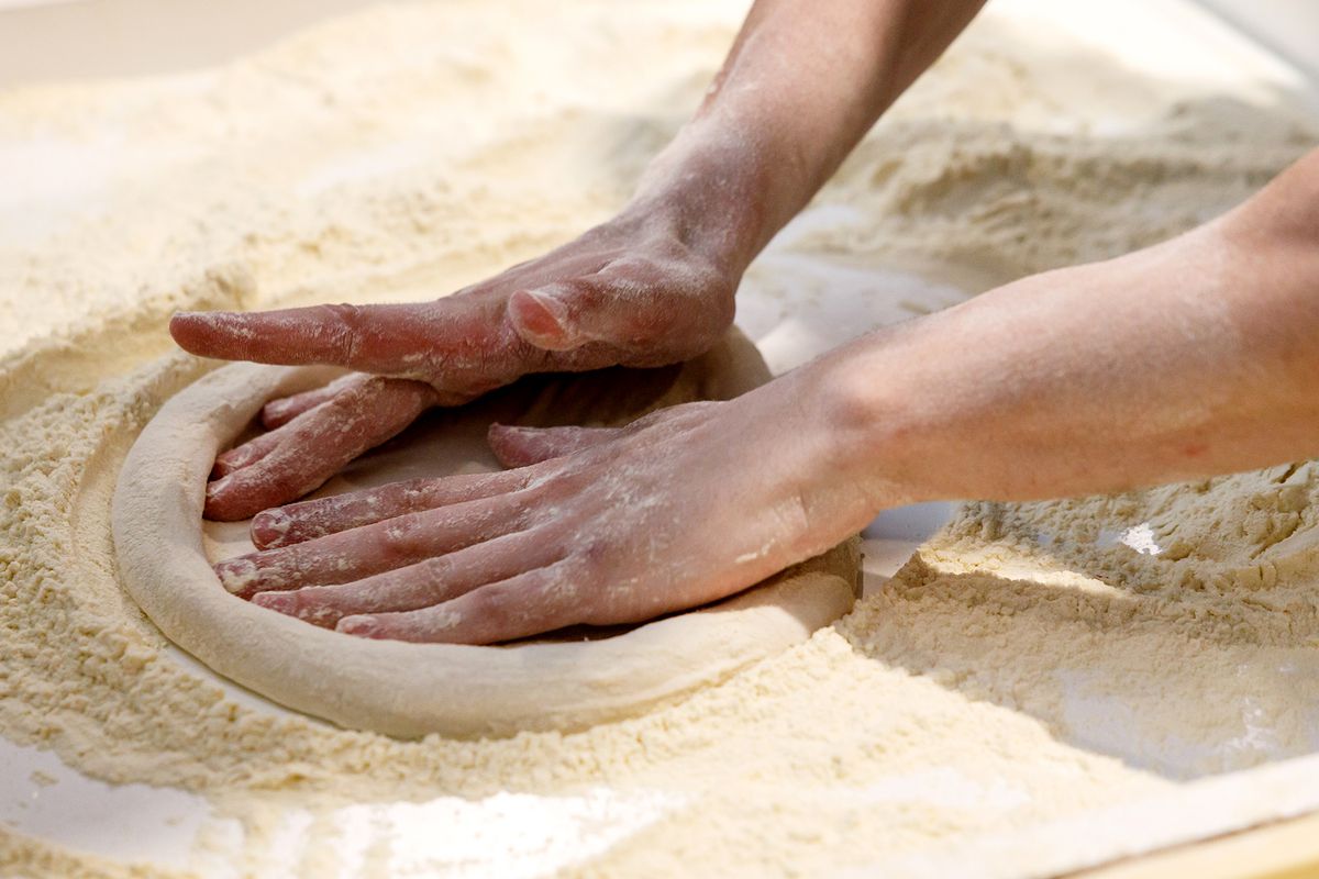 A baker kneads dough on a well floured surface. 