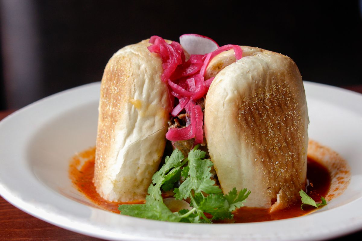 A sliced in half sandwich stuffed with beef and red pickled onions sits on its side in a low-edged bowl