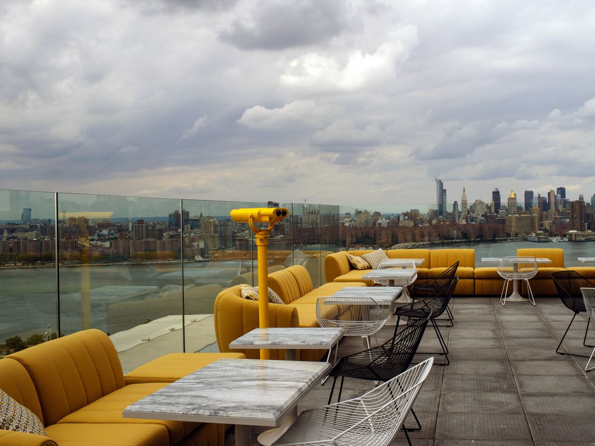 A rooftop bar with yellow couches shows off city views.
