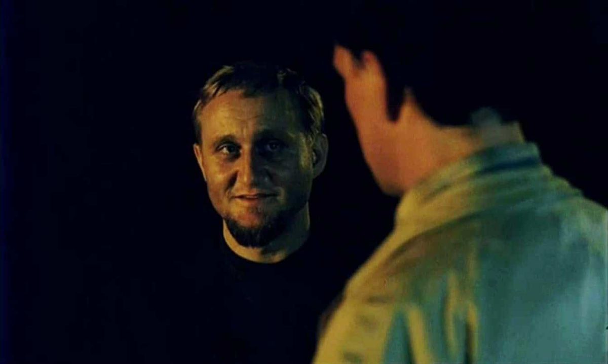 A sinister-looking man with a goatee smiles at another man against a pitch-black background in The Vanishing.