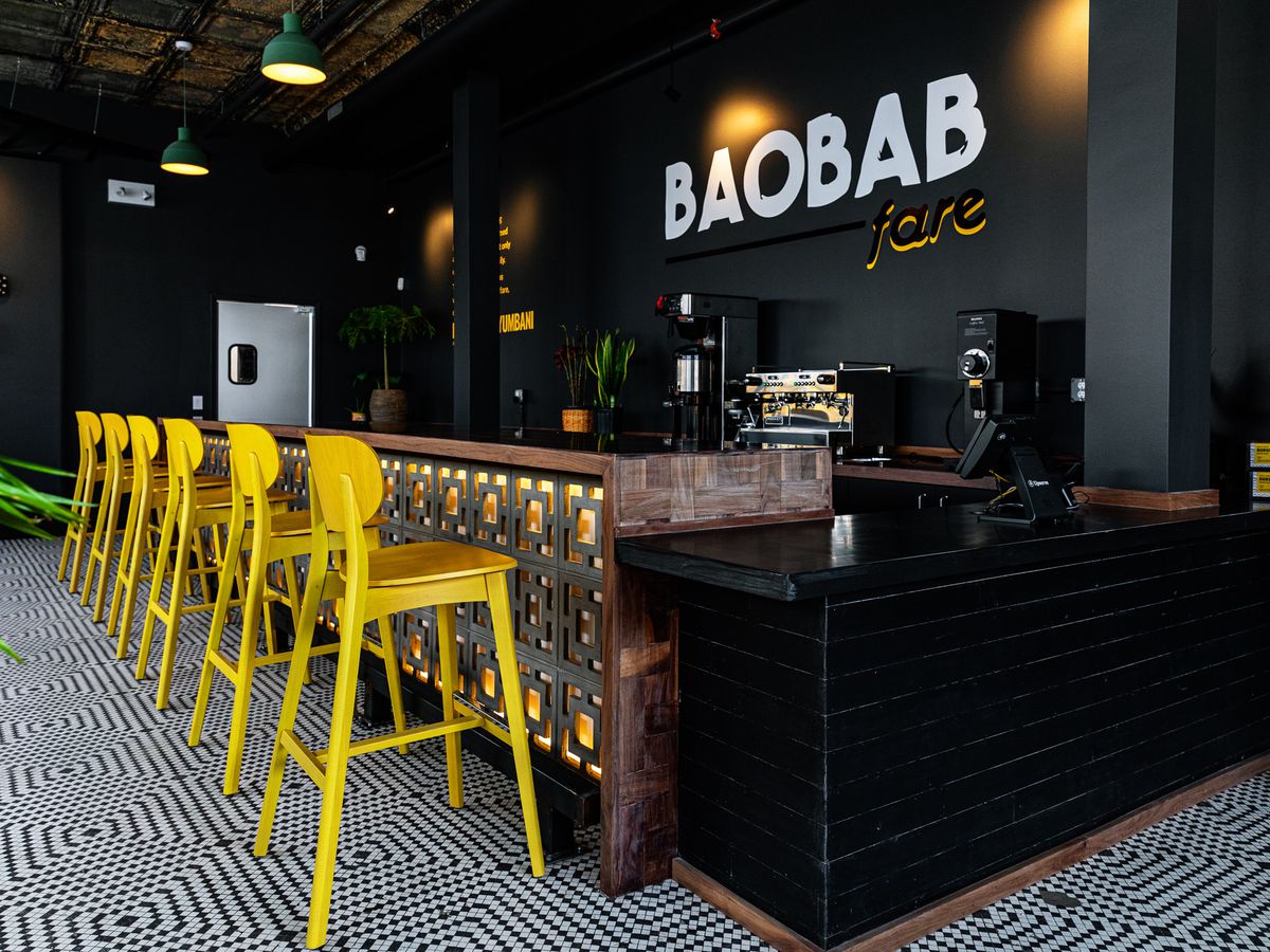 A shot looking down the bar at Baobab Fare with six bright yellow bar stools set atop a blue and white tile floor.