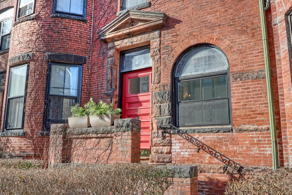 A closeup of the exterior of a brick rowhouse with a red front door.
