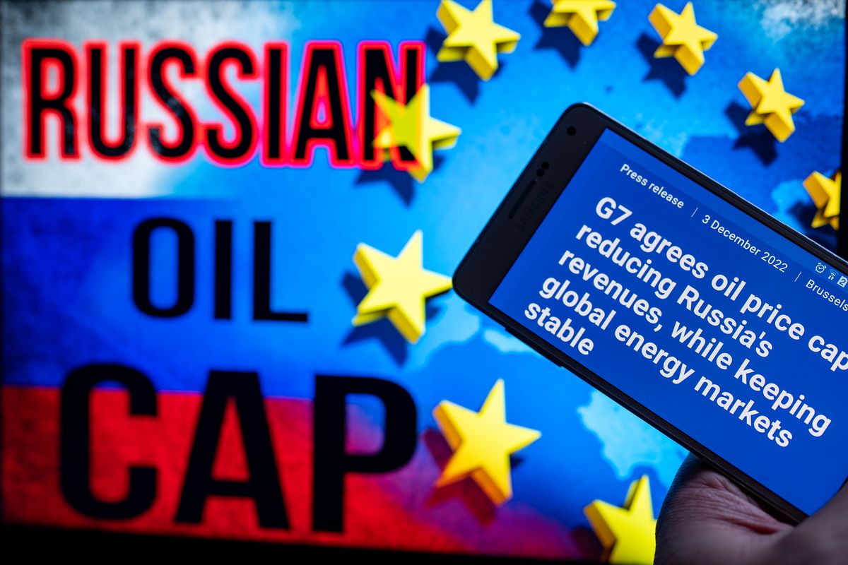 Photo illustration of the EU logo with the Russian flag on a screen with a mobile device reading the EU Commission’s press release, “EU agrees $60 price cap on Russian oil.”