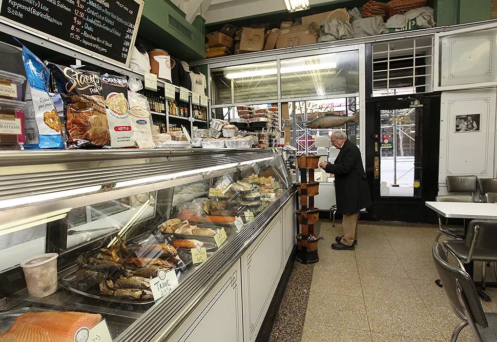 The interior of Barney Greengrass with a man waiting to order food. The refrigerated counter showcases the different meats and spreads the establishment has to offer.