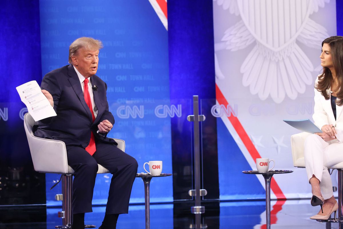 Former President Donald Trump sitting onstage, showing the interviewer a piece of paper.