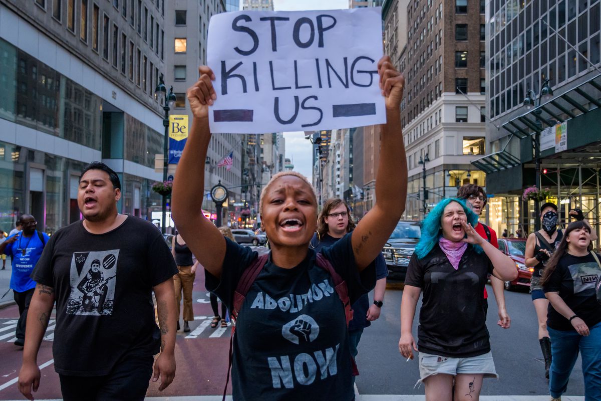 A protester marching with others on a New York street holds a sign overhead that reads, “Stop killing us.”