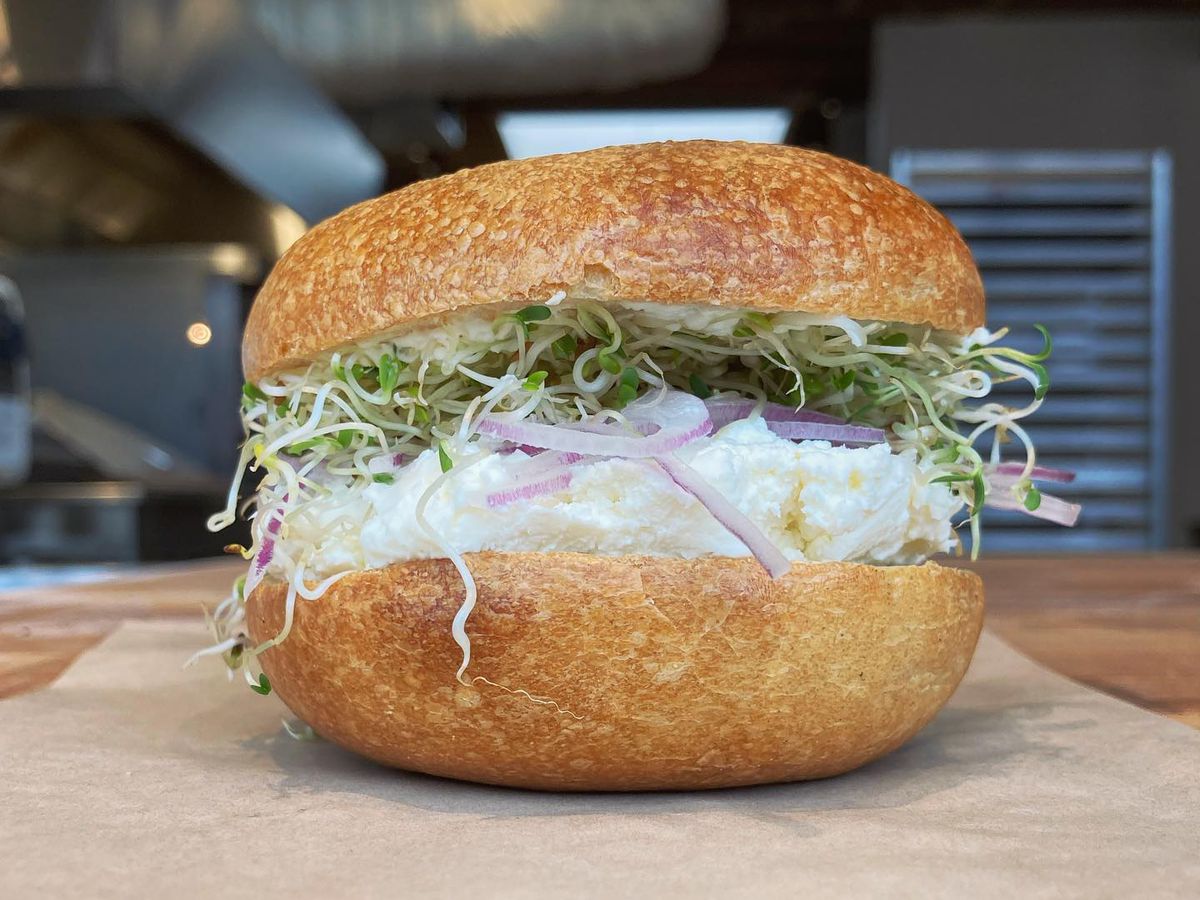 A bagel sandwich with cream cheese, onion, and sprouts.